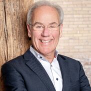 smiling older gentleman smiles at the camera, wearing a dark suit and white shirt